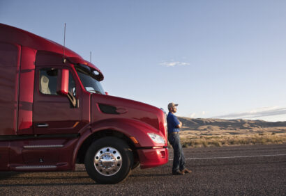Truck driver leaning on the grill of his commercial truck.